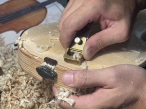 Luthier hand-graduating the inside of a cello plate with a thumb plane