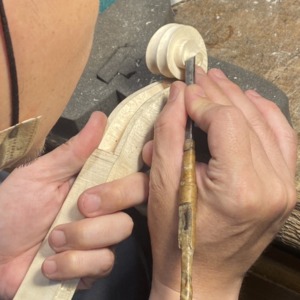 Luthier carving a cello scroll by hand at the workbench